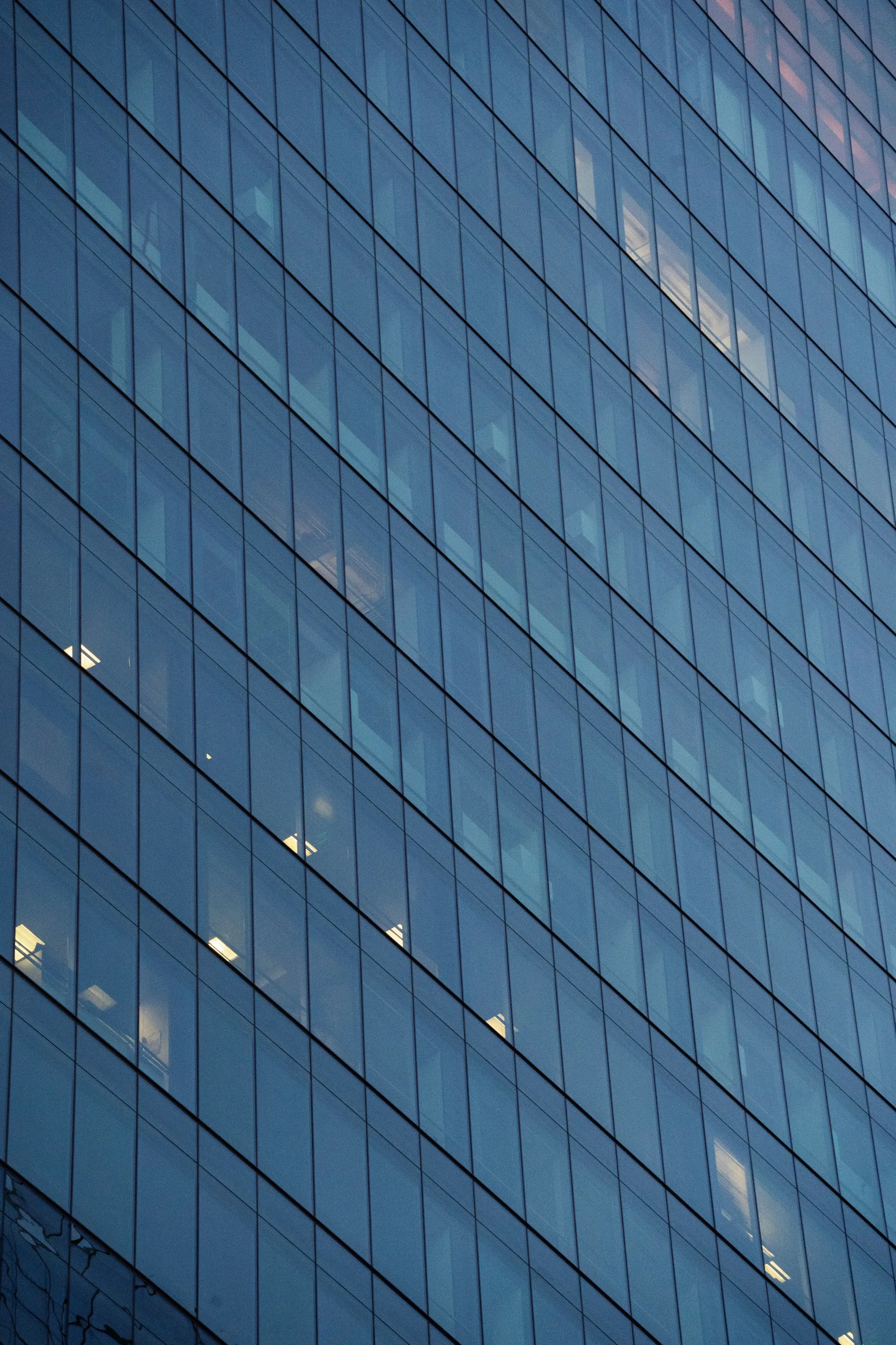 Fachada de vidrio de un edificio corporativo con luces interiores encendidas al atardecer